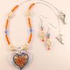 Beautiful glass heart embedded with a "mum" flower in peachy orange.  and a blue background enhanced with blue iridescent facet bicone crystals.  Orange bicones and creamy white acrylic beads enhanced with silver bead caps and an antique silver heart clasp compete this set with matching earrings.  The tiny twisted :"liquid silver" tube beads are sterling silver.  Necklace from fluted silver bead cap to bead cap is approx.  17 1/2" around.  Glass heart pendant is approx. 1 1/2" wide and 1 3/4" long including glass "hole."   Earring pendants are approx. 1 1/2" long.